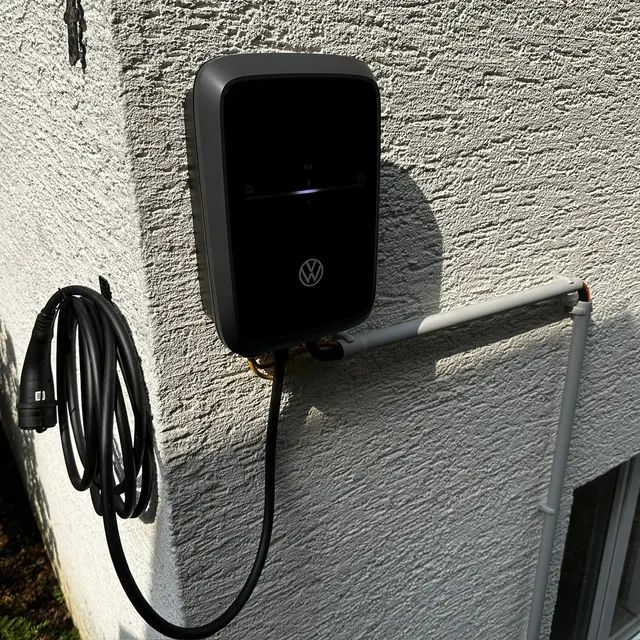 An der Außenwand montierte Wallbox mit angeschlossenem Ladekabel, das Kabel sauber aufgerollt daneben